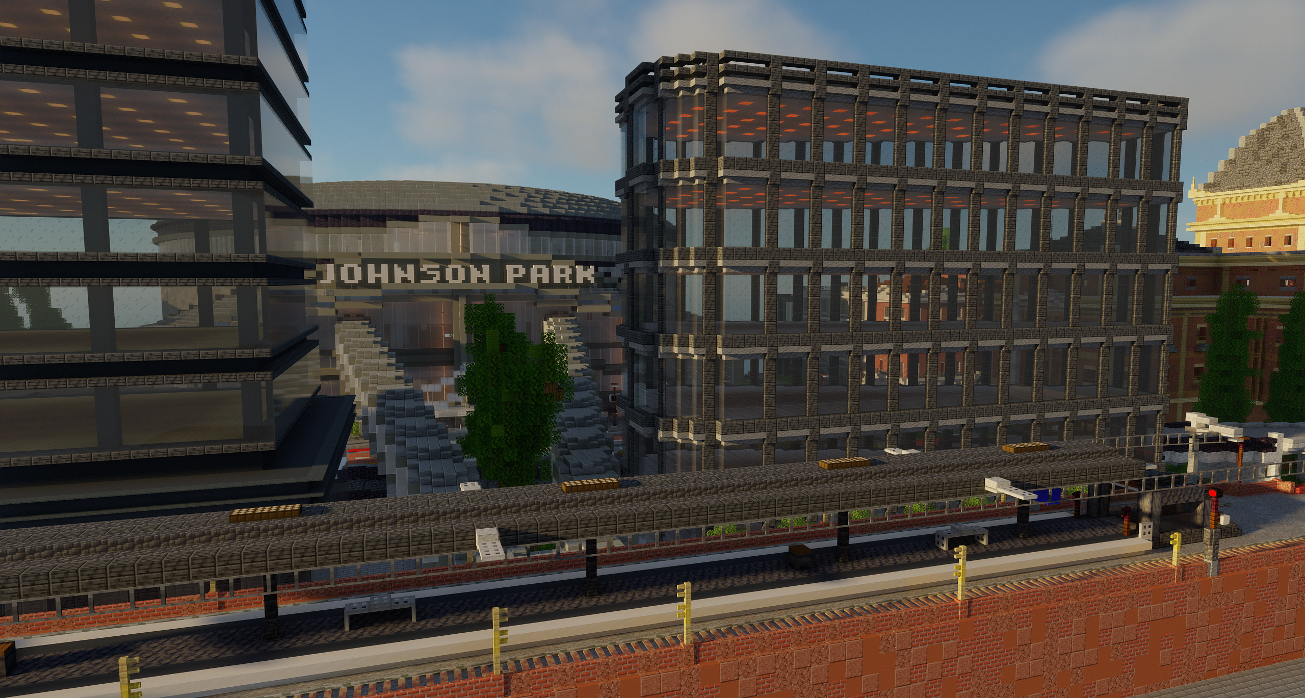 An image of Johnson Park station looking towards Johnson Park Hockey Stadium. Several tall buildings can be seen in the area behind the station and two elevated pedestrian walkways can be seen linking the station to the stadium.